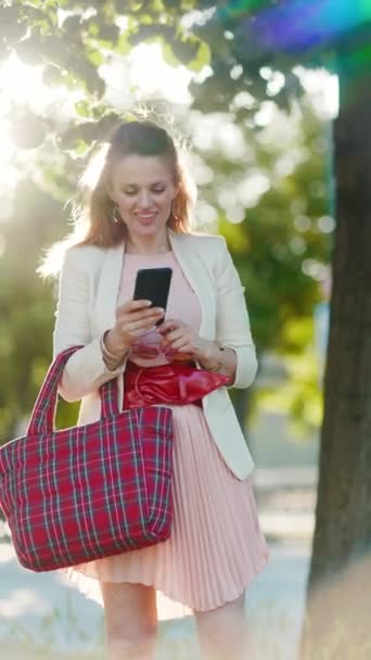 Zbliżenie Kobietę Różowej Sukience Białej Kurtce Mieście Smartfonem Czerwoną Torbą — Wideo stockowe