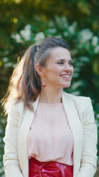 Усміхнена Елегантна Жінка Рожевій Сукні Білій Куртці Місті Проти Зелені — стокове відео