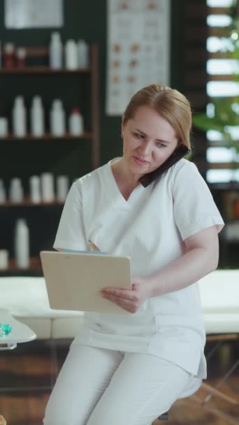 卫生保健时间 在温泉沙龙微笑的按摩师女人 带着剪贴板在智能手机上聊天 — 图库视频影像