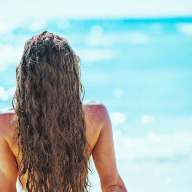 Deniz kenarında oturan genç bir bayan. arka görünüm