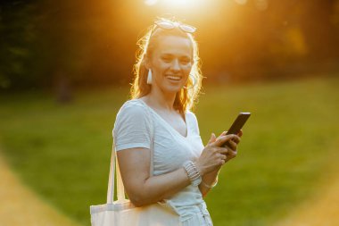 Yaz zamanı. Şehir parkındaki çayırda beyaz tişörtlü, akıllı telefon kullanan 40 yaşında mutlu bir kadın..