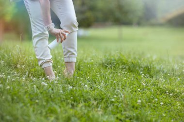 Yaz zamanı. Doğanın dışındaki çayırlarda püskürtücü sprey sıkan beyaz gömlekli modern kadına yakın çekim..