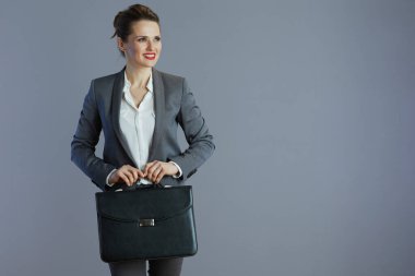 Gri arka planda izole edilmiş evrak çantası olan gri takım elbiseli, mutlu, küçük işletme sahibi kadın..