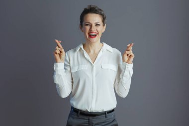 Mutlu, orta yaşlı, beyaz bluzlu küçük işletme sahibi kadın. Gri arka planda parmaklarını çapraz yapmış..