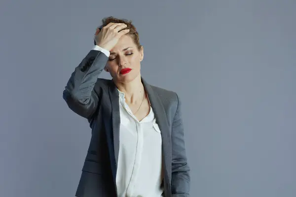 stressed trendy small business owner woman in gray suit against gray background.