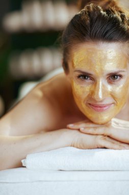 Sağlık hizmeti zamanı. Masaj maskesinin üzerinde altın kozmetik maskesiyle spa salonundaki rahat modern kadın..