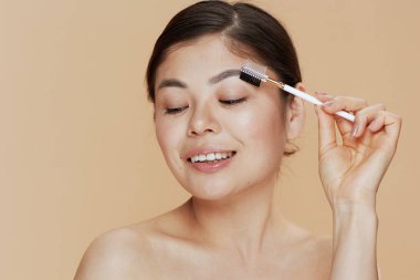 Bej arka planda kaş fırçası olan genç Asyalı kadın..