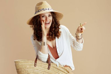 Plaj tatili Beyaz bluzlu, bej arkaplanlı, saman çantalı ve yaz şapkalı 40 yaşında mutlu bir ev hanımı..