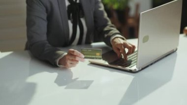 Sürdürülebilir iş yeri. Yeşil ofisteki gri takım elbiseli, dizüstü bilgisayarı ve kredi kartı olan küçük işletme sahibi kadına yakın plan..