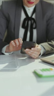 Sürdürülebilir iş yeri. Yeşil ofisteki gri takım elbiseli iş kadını akıllı telefon uygulamaları kullanıyor..