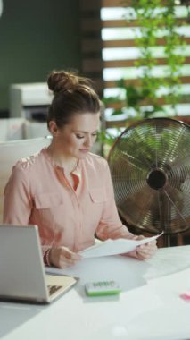 Sürdürülebilir iş yeri. Mutlu modern 40 yıllık kadın çalışan belgelerle ve elektrikli vantilatörle.