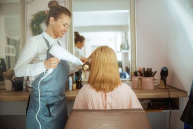 40 yaşında kadın kuaför, saç fırçası ve saç kurutma makinesi olan bir müşteri..