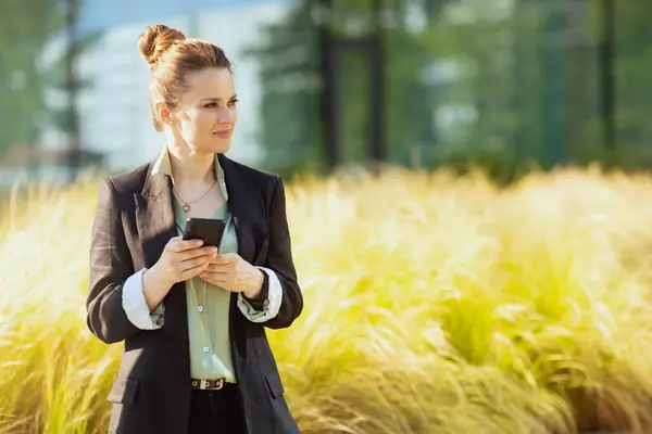 商务区内快乐的现代女性员工穿着黑色夹克 使用智能手机 图库图片