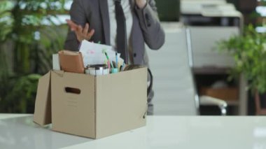 Yeni bir iş. Modern yeşil ofisteki, gri takım elbiseli, karton kutuda kişisel eşyaları olan, akıllı telefondan konuşan modern kadın işçiyi strese sokuyorum..