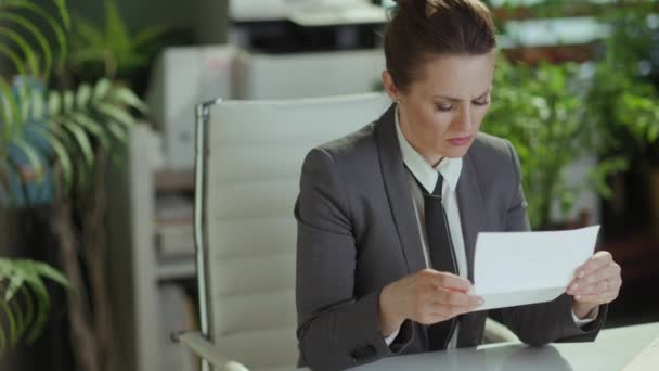 新しい仕事 不幸な現代40歳の女性労働者 従業員の終了の手紙が付いている灰色のビジネス スーツの現代緑のオフィスで — ストック動画