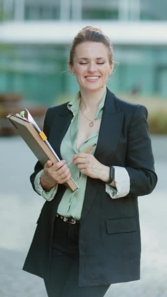 文書およびフォルダが付いている黒いジャケットのビジネス センターの近くの現代中年のビジネス 女性微笑 — ストック動画