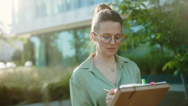 穿着绿色衬衫和眼镜 头戴文件和文件夹 在商业中心附近沉思的现代中年女商人 — 图库视频影像