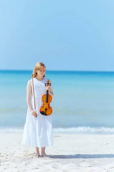 バイオリンで海岸の白いドレスで現代の若い女性を笑顔にする完全な長さの肖像画 — ストック写真