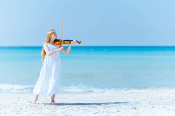 Full length portrait of modern young woman in light dress with violin enjoying playing on the seacoast.