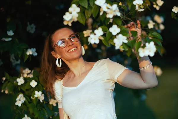 夏天的时候快乐的现代女人 身穿白衬衫 眼镜紧盯着开花的树 — 图库照片