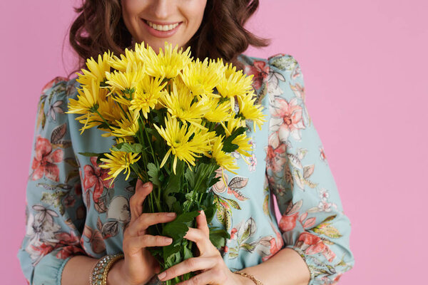 Closeup on smiling middle aged woman with long wavy brunette hair with yellow chrysanthemums flowers isolated on pink.