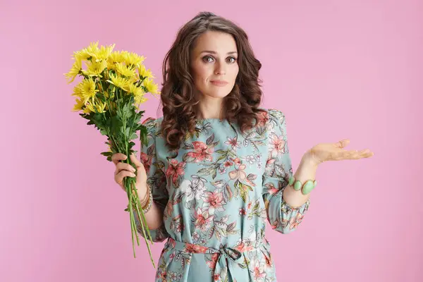 ピンクの背景にふさわしい黄色の菊花の花と花のドレスでスタイリッシュな女性 ストックフォト