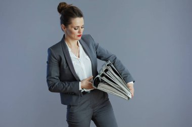 Gri arka planda klasörleri olan, gri takım elbiseli, orta yaşlı, modaya uygun, küçük işletme sahibi bir kadın..
