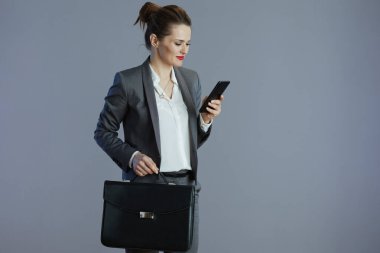 Mutlu, orta yaşlı, gri takım elbiseli, gri arka planda çantalı küçük işletme sahibi kadın..