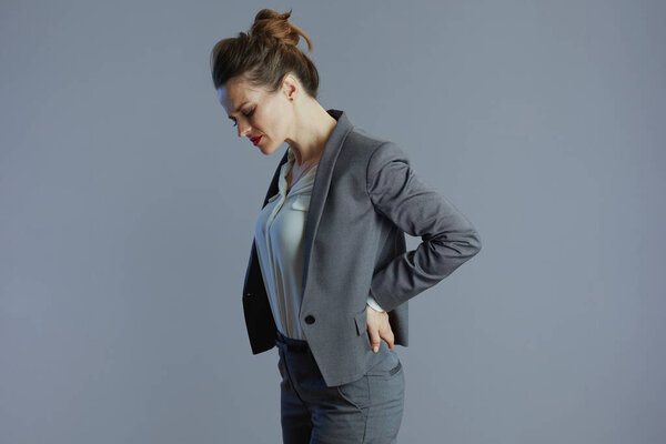tired elegant 40 years old woman employee in grey suit having back pain isolated on grey background.