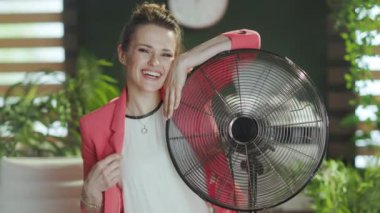 Sürdürülebilir iş yeri. Gülümseyen modern 40 yaşındaki muhasebeci kadın elektrikli yelpazeli kırmızı ceketli..