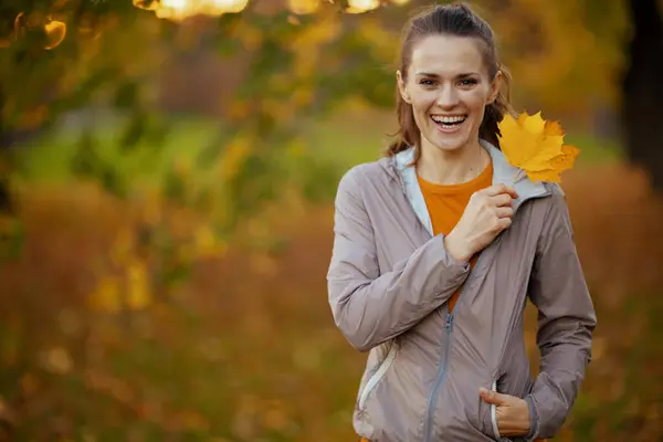 Hello autumn. Portrait of happy elegant female in fitness clothes in the park with autumn leaf.