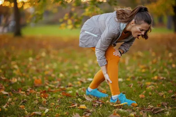公园里穿着健美衣服的不快乐的中年妇女脚踝酸痛 — 图库照片