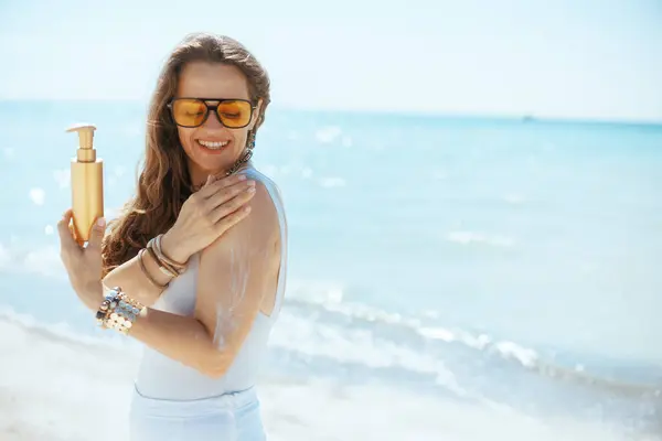 快乐的现代女子在海滨用防晒霜 图库照片
