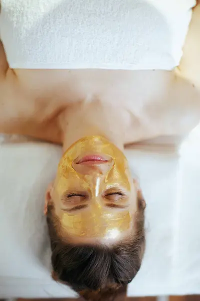 卫生保健时间 浅谈躺在按摩床上 头戴金色化妆品面具的现代女性放松的上观 图库图片