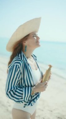 Gülümseyen stil sahibi kadın deniz kıyısında spf ile.