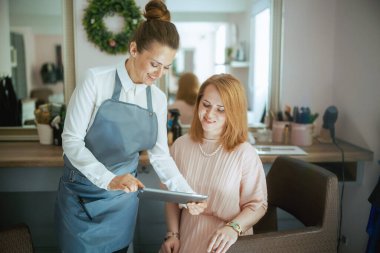 Modern saç stüdyosunda tableti ve müşterisi olan kadın kuaför..