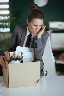 Yeni bir iş. Mutsuz modern 40 yaşında, modern yeşil ofis çalışanı gri takım elbiseli, karton kutuda kişisel eşyaları olan..