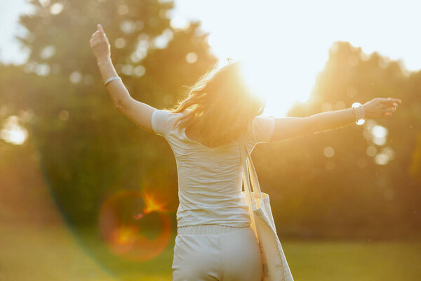 Летнее время. Улыбающаяся 40-летняя женщина в белой рубашке с сумкой на лугу на природе.