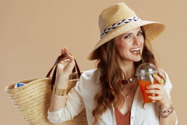 Plaj tatili Beyaz bluz giyen zarif bir bayan ve bej arka planda saman torbası, havuç suyu ve yaz şapkası olan şortlu bir kadın..