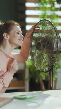 Sürdürülebilir iş yeri. Gülümseyen modern 40 yaşındaki kadın çalışan elektrikli yelpazeyle çalışıyor..