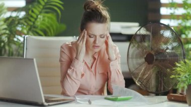 Sürdürülebilir iş yeri. Mutsuz modern kadın işçi elektrikli vantilatörle çalışıyor.