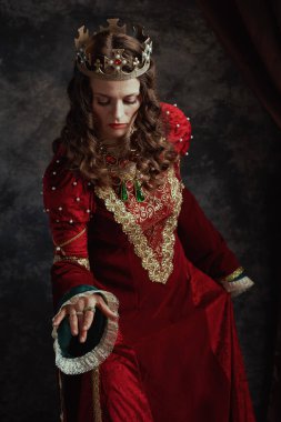 Kırmızı elbiseli ortaçağ kraliçesi koyu gri arka planda saygı gösteriyor..