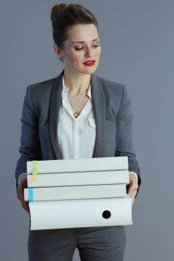 40 yaşında, gri takım elbiseli, gri arkaplanda klasörleri olan küçük işletme sahibi bir kadın..