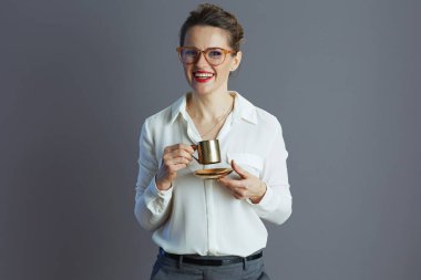 Gri renkli bardakları ve kahve fincanlarıyla beyaz bluzlu, güler yüzlü moda bir kadın işçi..