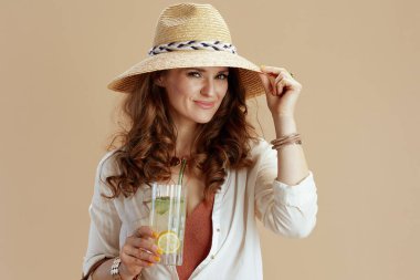 Plaj tatili Beyaz bluzlu ve şortlu zarif bir kadın. Kokteyl ve yaz şapkalı bej üzerine izole edilmiş..
