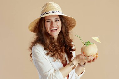 Plaj tatili Beyaz bluz ve şortlu, hindistan cevizi kokteyli ve hasır şapkalı bej üzerine izole edilmiş, güler yüzlü 40 yaşındaki ev kadını..