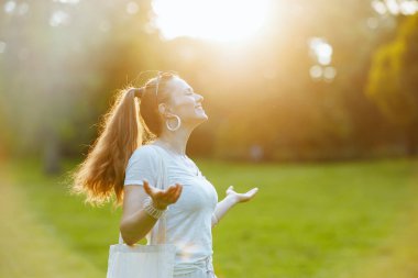 Yaz zamanı. Mutlu modern 40 yaşındaki beyaz gömlekli kadın doğanın dışındaki çayırlarda eğleniyor..