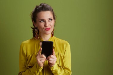 Yeşil arka planda izole edilmiş yeşil bluzlu, akıllı telefon kullanan, güler yüzlü bir kadın..