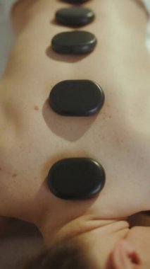 Sağlık hizmeti zamanı. Sıcak taş masajı yaptıran ve masaj masasına uzanan rahat, modern bir kadına yakın çekim..