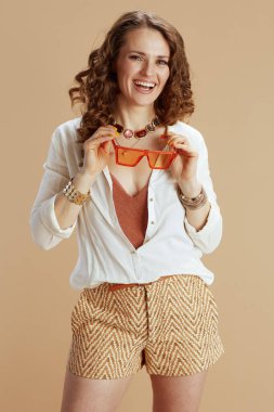 Plaj tatili Beyaz bluzlu zarif bir bayan ve bej arkaplanda güneş gözlüklü bir şort..